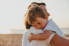 2 year old boy hugs mom in a beach